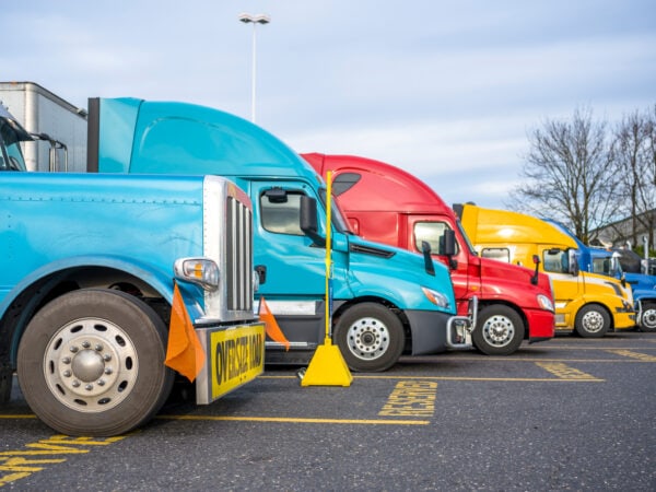 Different big rigs semi trucks with semi trailers standing in row on truck stop parking lot with reserved spots for truck driver rest and compliance with established truck driving regulations"n